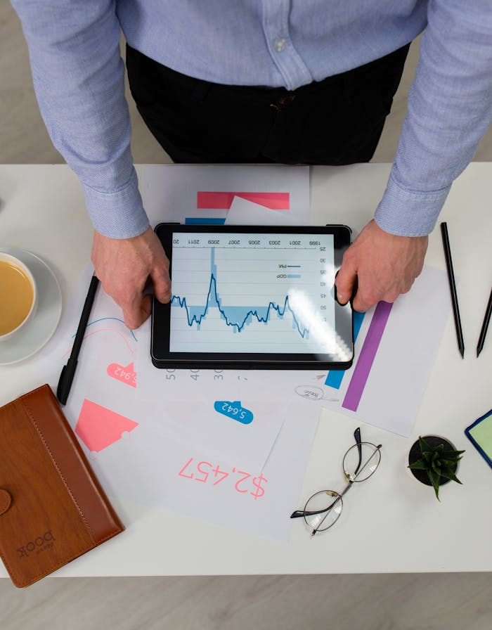About Top view of a professional analyzing financial data on a tablet at a desk.